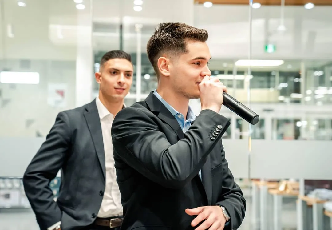 Nicolas Buffone speaking into a microphone at an Expandify event, with Jonathan Durante behind him